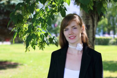 Siyah ceketli oldukça gülümseyen kadın pozlar güneşli yeşil Park'ta bir