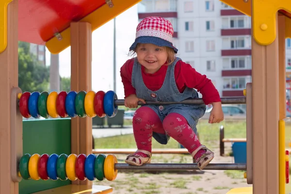 Little pretty girl in hat climbs on children playground at sunny — Stock Photo, Image