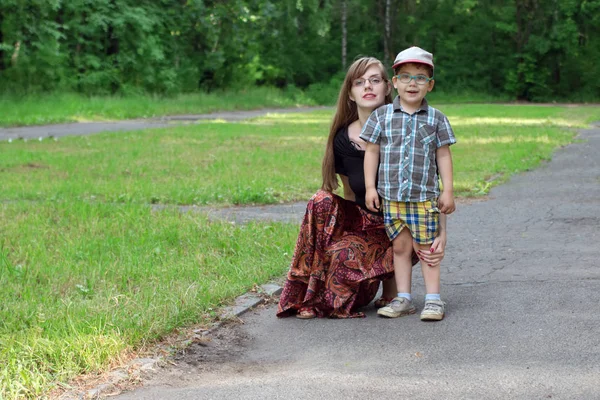 Piccolo bel ragazzo e la sua giovane madre posare nel parco al sole d — Foto Stock