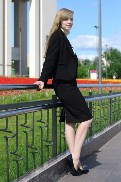 Krásná žena v černém obleku představuje poblíž zábradlí ve slunném městě — Stock fotografie