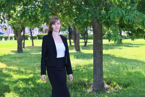 Pretty young woman in black suit poses in sunny green park at su — Stock Photo, Image