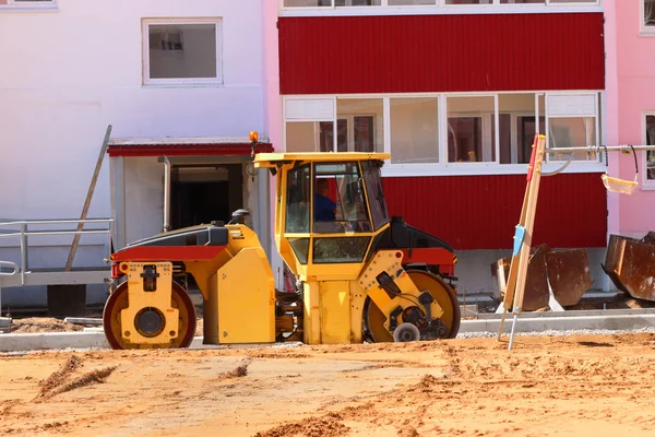 Gran rodillo en el sitio de construcción junto a un nuevo edificio y playgro Imagen de stock