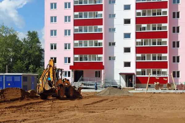 Tractor trabaja cerca de nuevo edificio en el sitio de construcción en verano s Imagen de archivo