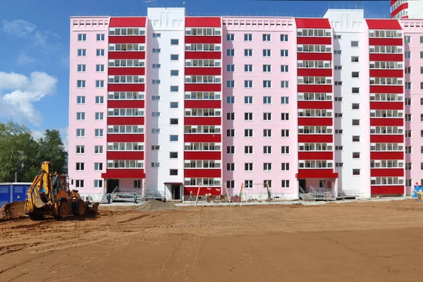 Tractor trabaja cerca de nuevo edificio rosa en el sitio de construcción en suma Fotos de stock libres de derechos