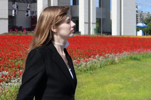 Красива молода жінка в чорній куртці позує біля червоної клумби в Ліцензійні Стокові Зображення