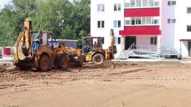 İki sarı traktör inşaat sitesinde yaz gününde çalışmak.