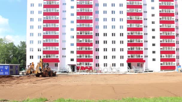 Gelber Traktor arbeitet an Sommertag nahe rosa Gebäude auf Baustelle — Stockvideo