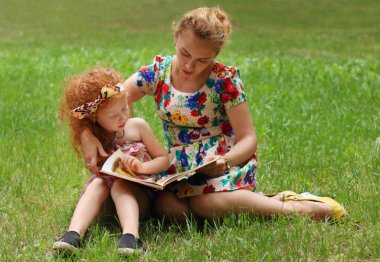 Küçük kız ve annesi çim yaz Park, sha kitap okumak