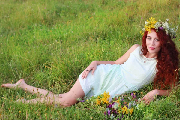 Barfüßige Frau in Kranz und kurzem Kleid liegt im Gras auf Wiese — Stockfoto