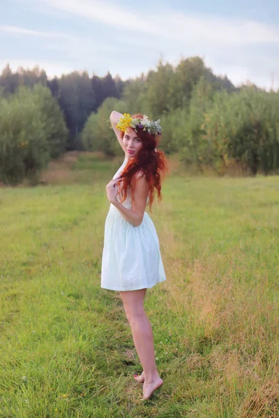 Pretty barefoot woman in wreath and short dress poses on meadow — Stock Photo, Image