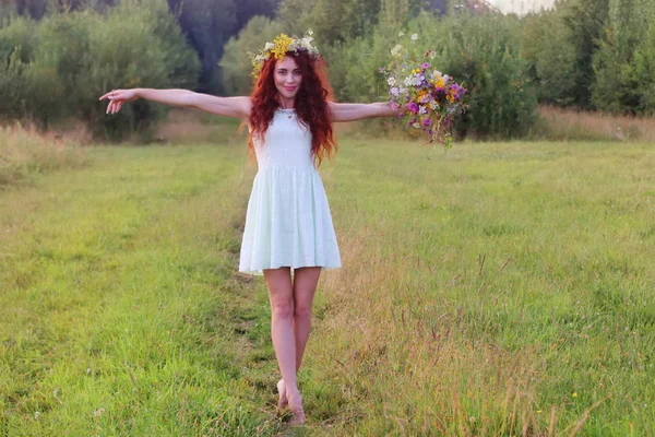 Barefoot woman in wreath with bunch of flowers on meadow at summ — Stock Photo, Image