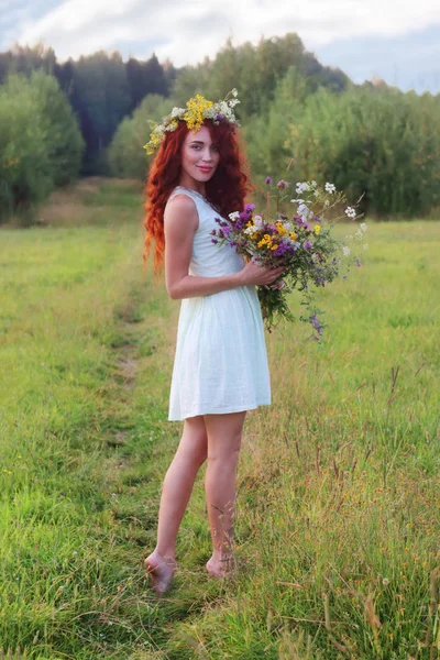 Woman in wreath with bunch of flowers on meadow at summer day — Stock Photo, Image