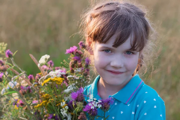 Küçük kız gülümser ve kır çiçekleri kuru alanında yaz tutar — Stok fotoğraf