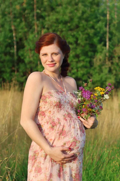 Beautiful pregnant woman with wild flowers touches belly at summ — Stock Photo, Image