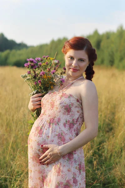 Beautiful pregnant woman poses with wild flowers at summer day o — Stock Photo, Image