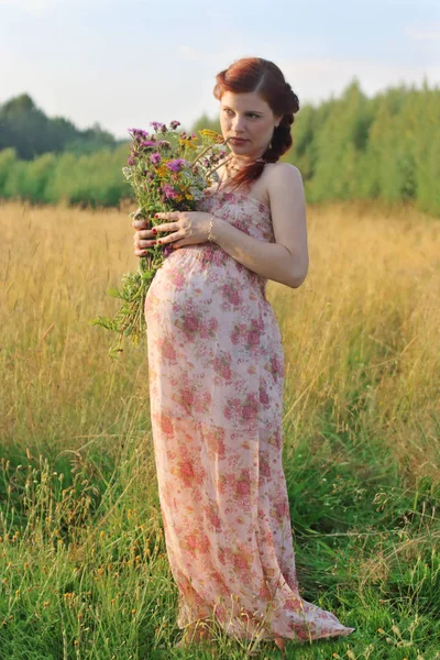 Pretty pregnant woman poses with wild flowers at summer day outd — Stock Photo, Image