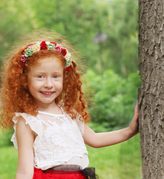 Bambina con fiori ghirlanda si trova vicino a grande albero in estate p — Foto Stock