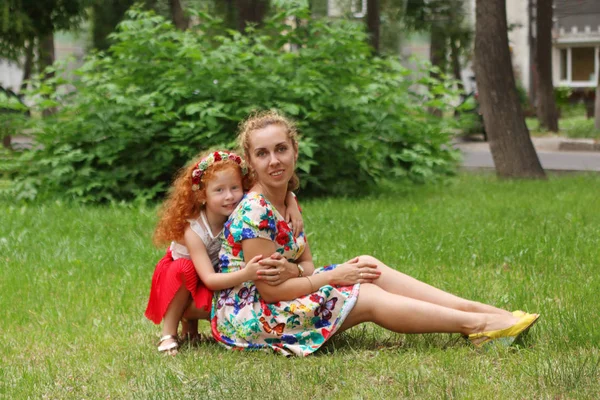 Little cute girl poses with her mother on lawn in summer park, s — Stock Photo, Image