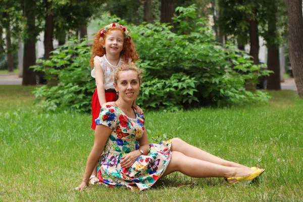 Malá holčička představuje se svou matkou na trávníku v letním parku, shallo — Stock fotografie