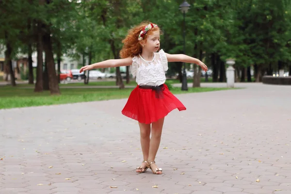 Little girl with red hair dances in green summer park, shallow d — Stock Photo, Image