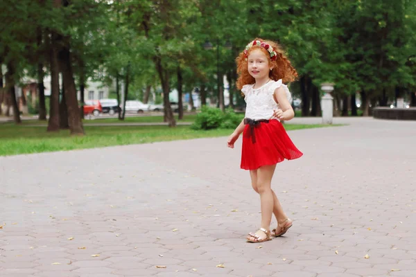 Little smiling girl with red hair walks in green summer park, sh — Stock Photo, Image