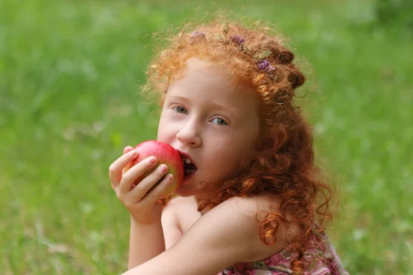 Mała dziewczynka zjada apple na trawnik w parku Zielona letnia, bliska, s — Zdjęcie stockowe