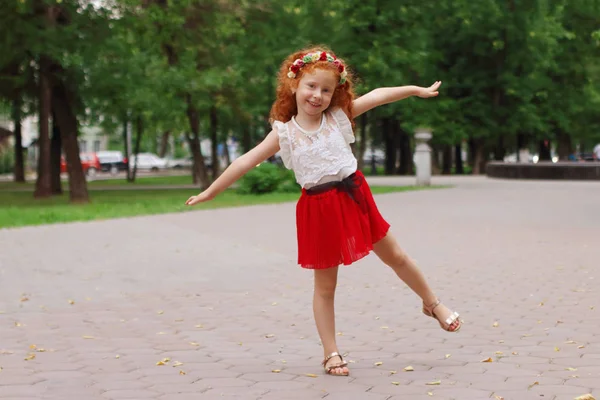 Little smiling girl with red hair poses in green summer park, sh — Stock Photo, Image