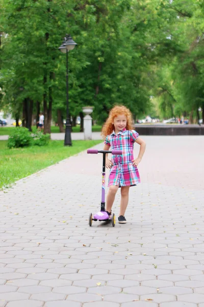 Glückliches kleines Mädchen mit roten Haaren posiert mit Roller im Sommer par — Stockfoto