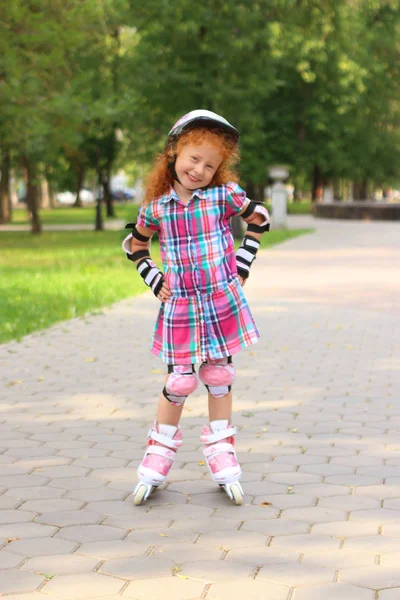 Lächelndes kleines Mädchen mit Helm auf Rollschuhen im grünen Sommerpark — Stockfoto