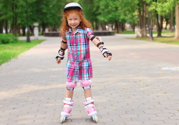 Petite fille mignonne en patins à roulettes casque dans le parc d'été vert — Photo