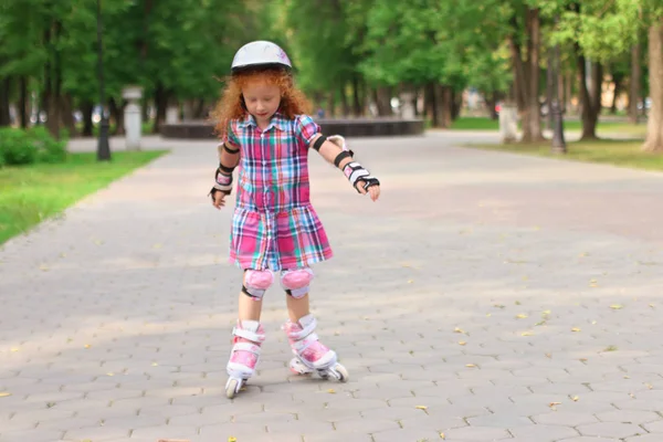 Funny little girl in helmet roller skates in green summer park — Stock Photo, Image