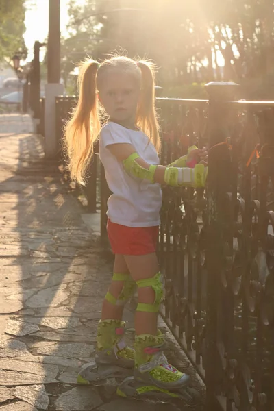 Little girl on roller skates poses near railing in sunny summer — Stock Photo, Image