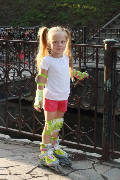 Carino bambina sui pattini a rotelle posa vicino ringhiera in estate p — Foto Stock