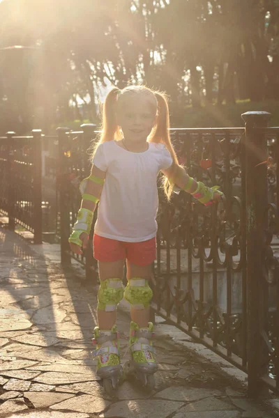 Cute little girl on roller skates poses near railing in sunny su — Stock Photo, Image