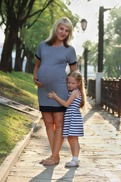 Pregnant mother and her little happy daughter stand in sunny par — Stock Photo, Image