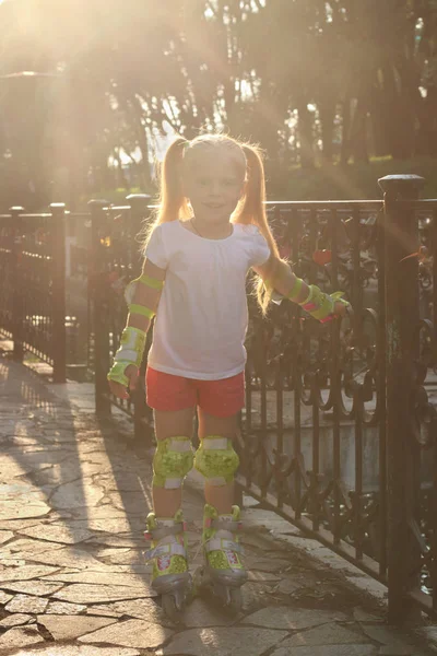 Cute little girl on roller skates poses near railing in sunny su Royalty Free Stock Photos