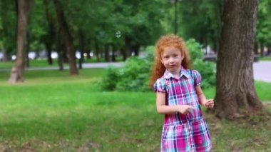 Kızıl saçlı sevimli küçük kız yeşil yaz park kabarcıkları yakalar