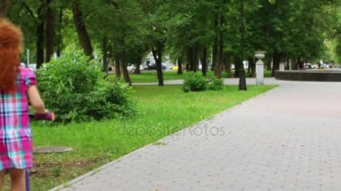 Sevimli küçük kız rides scooter yeşil yaz Park, arkadan görünüm