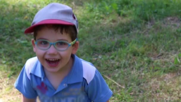 Счастливый милый мальчик в очках и кепке смеется, замедленная съемка — стоковое видео