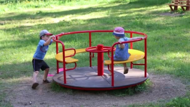 Gelukkig weinig jongen en meisje spelen met carrousel in zomer groen park — Stockvideo