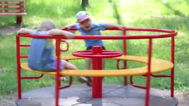 Happy little boy and girl have fun on carousel in summer green park — Stock Video