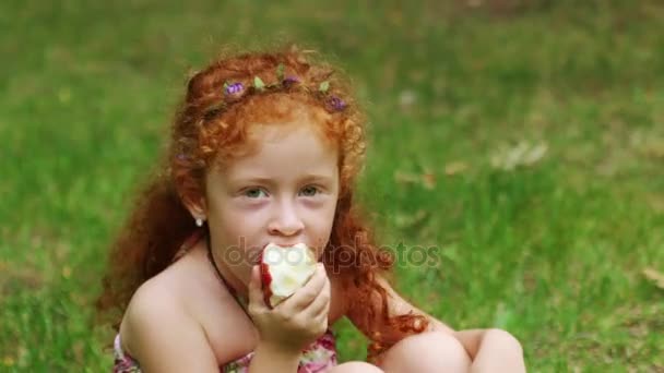 Meisje eet appel op gazon in groene zomer park, close-up — Stockvideo