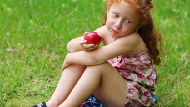 Bonne petite fille mange pomme sur la pelouse dans le parc d'été vert 