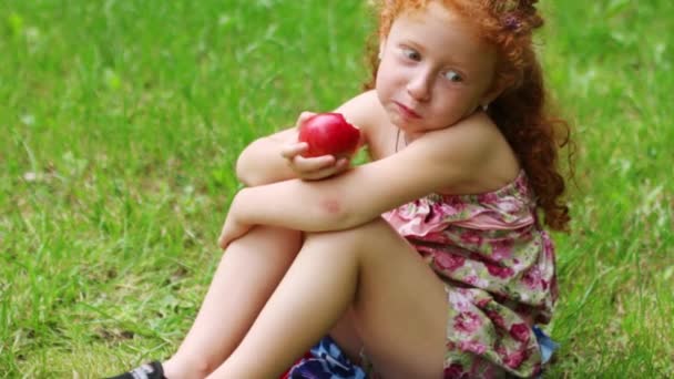 Menina feliz come maçã no gramado no parque de verão verde — Vídeo de Stock