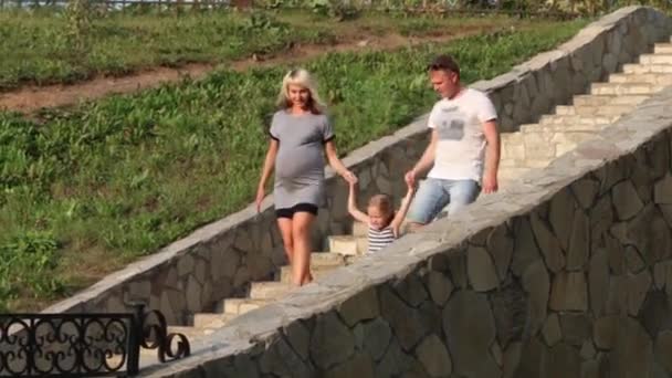 Madre embarazada, padre, hija feliz bajando escaleras en el parque de verano — Vídeos de Stock