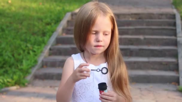 Pequena menina bonito sopra bolhas perto de escadas no parque ensolarado verde — Vídeo de Stock
