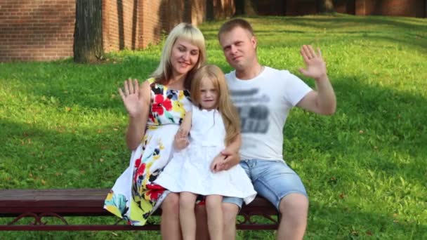 Gravid mor, far, lilla dotter våg händer på bänk i sommaren park — Stockvideo