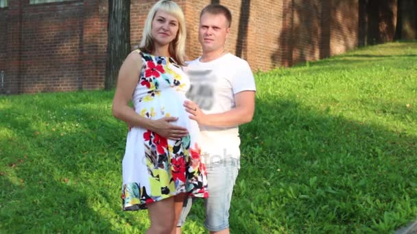 Беременная женщина и счастливый мужчина позируют в летнем зеленом парке — стоковое видео