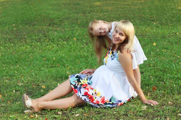 Happy little girl and pregnant mother pose on green grass in sum — Stock Photo, Image