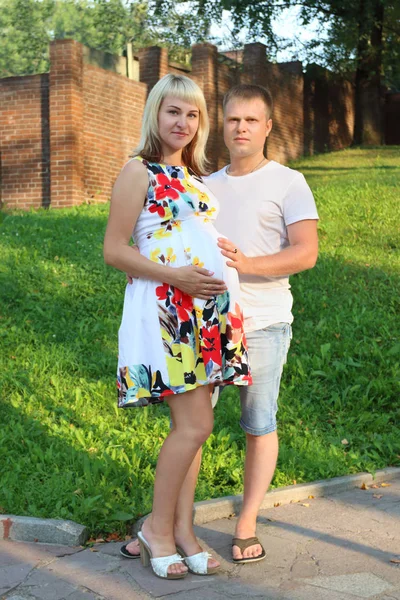 Pregnant woman and young man pose in summer sunny park — Stock Photo, Image